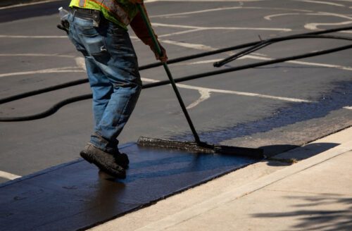 Man using a sealcoating brush to spread asphalt on a parking lot
