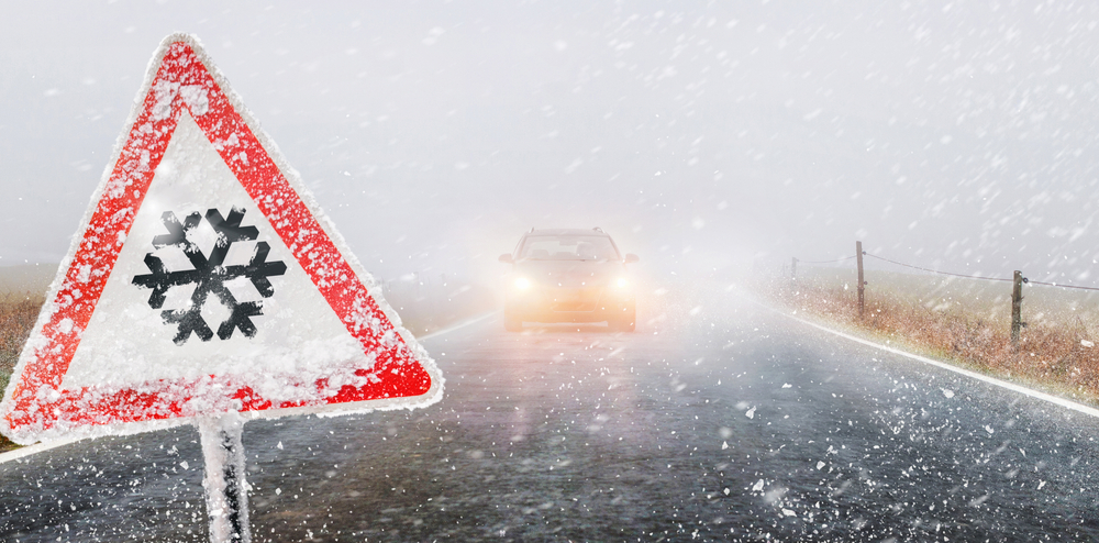 hazard sign with car driving in a snow storm