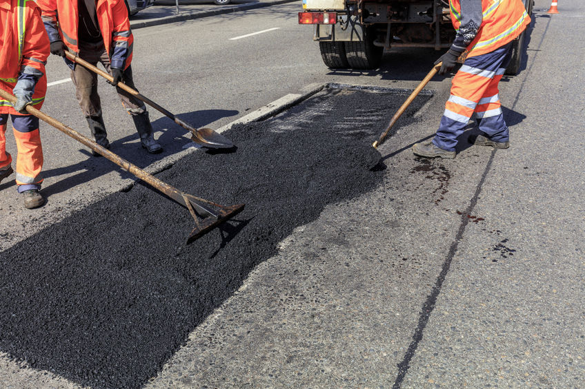 The working team of road builders distributes fresh asphalt on the road section and levels it for repair.